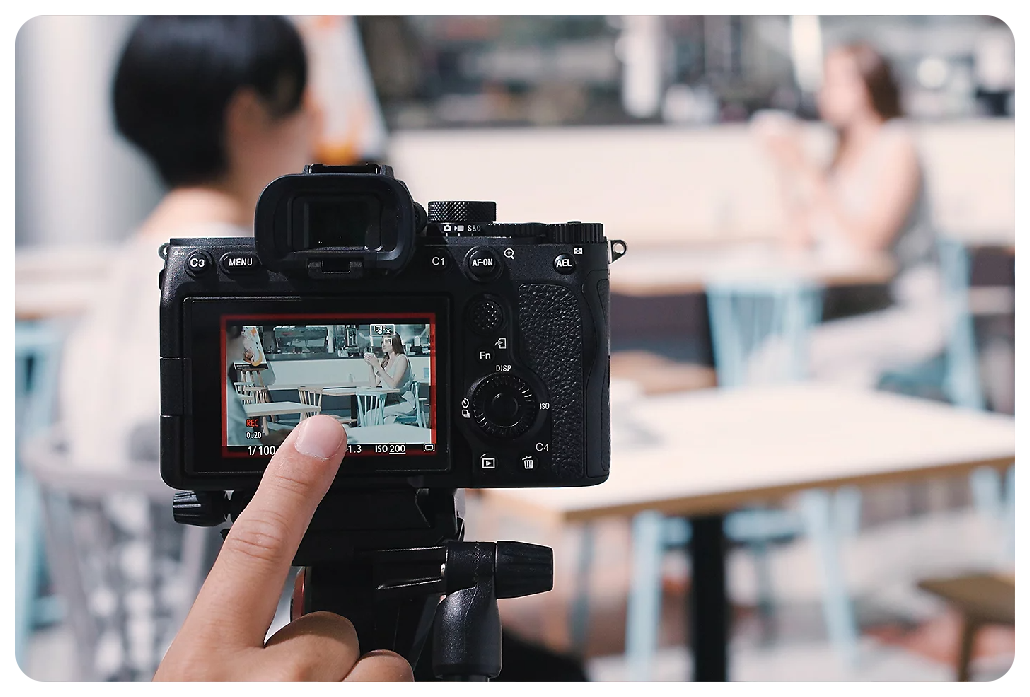 Sony A7 IV Camera on tripod capturing video of two people sat at cafeteria table